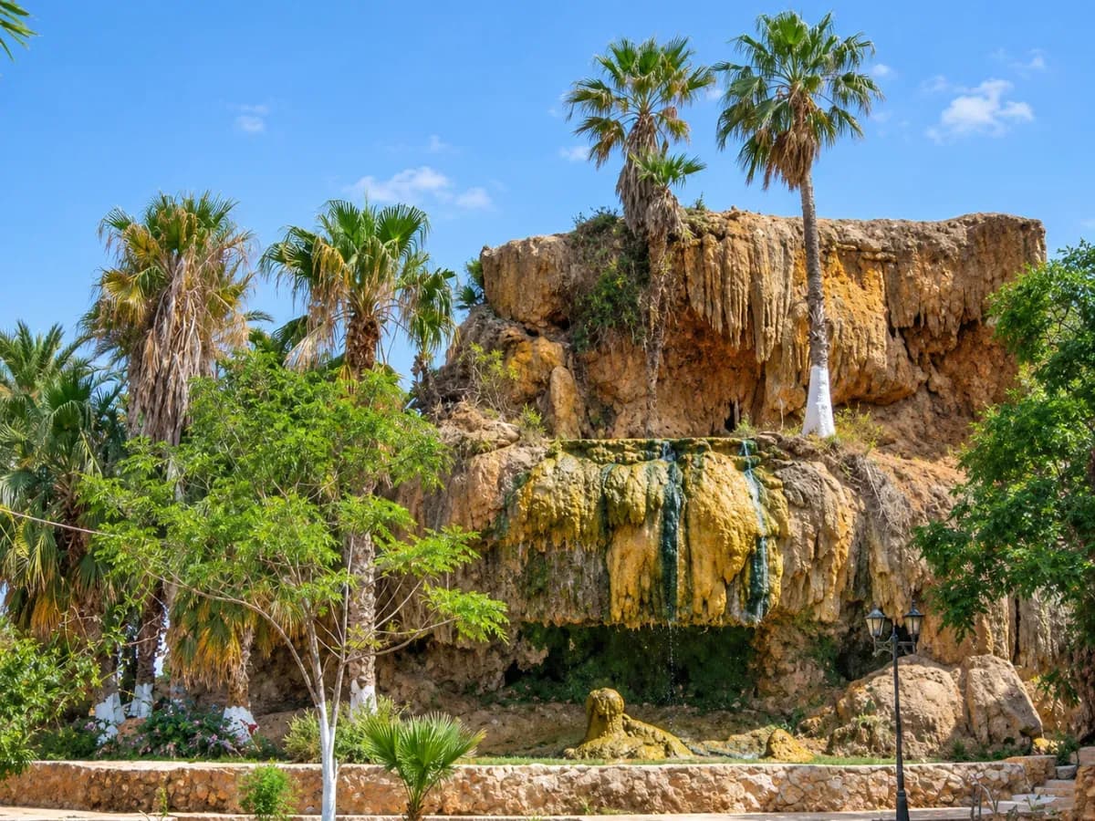 Cascade thermale du Hammam Bouhdjar, à Aïn Témouchent, entourée de formations rocheuses dorées et de palmiers.